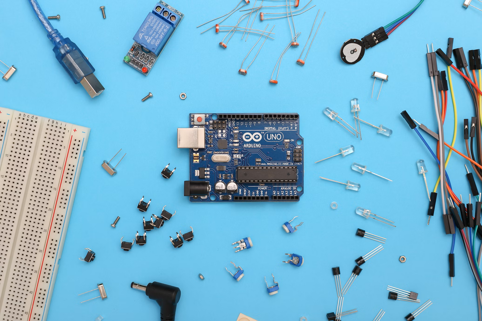 An image of an Arduino Uno microcontroller surrounded by various electronic components, such as LEDs, resistors, and jumper wires, used for DIY electronics projects